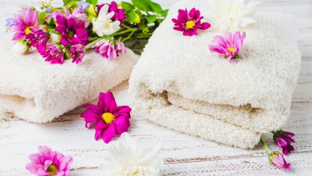 Two folded bath towels with some flowers on top